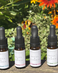 Four bottles of Angus & Florrie essential oils with droppers on a wooden surface against a natural background.