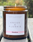 Candle in a brown jar with 'Angus & Florrie' label on a wooden surface