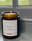 Candle in a jar with 'Angus & Florrie' label on a reflective surface