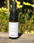 Bottle of Angus & Florrie essential oil on a wooden surface with flowers in the background