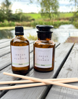 Two bottles of 'Angus & Florrie' product on a wooden table with a scenic background.