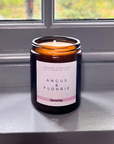 Candle in a glass jar with a label reading 'Angus & Florrie Serenity' on a reflective surface.