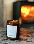 Candle in a brown jar with a label reading 'Angus & Florrie' on a rustic surface with a blurred background.