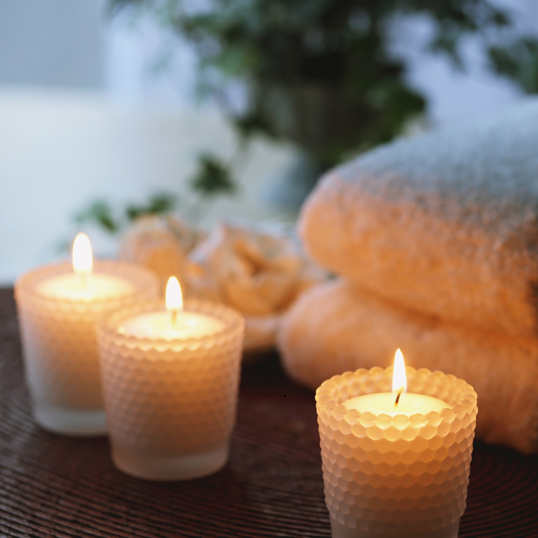 3 lit candles with towels & plants in the background