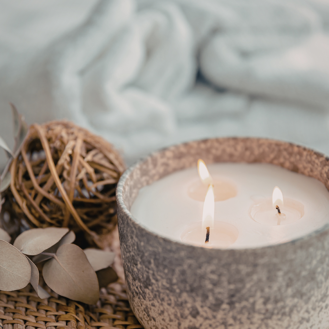 Candle with 3 wicks in stone jar, with blanket & leaves in background