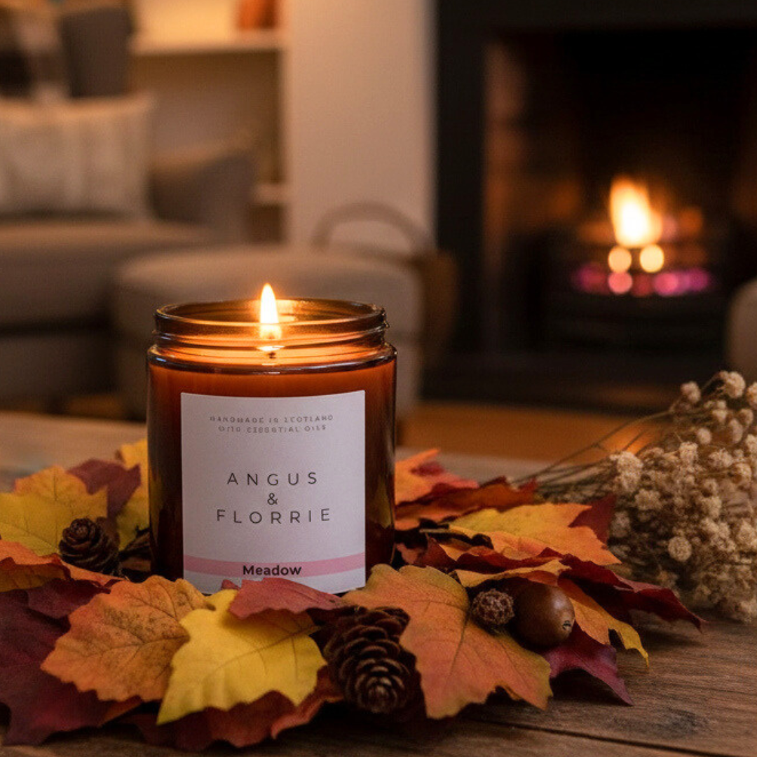 Candle labeled 'Angus &amp; Florrie' on a table with autumn leaves and a fireplace in the background