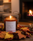 Candle labeled 'Angus & Florrie' on a table with autumn leaves and a fireplace in the background