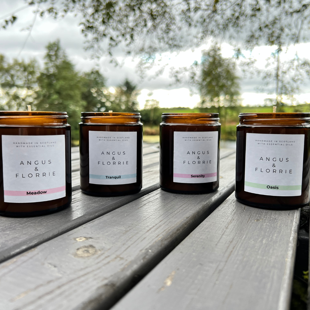 Four Angus &amp; Florrie candles on a wooden surface with a natural background