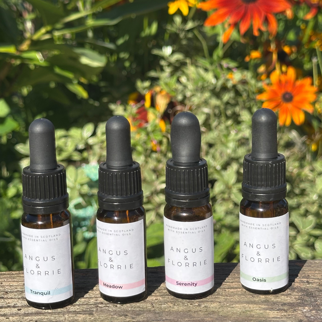 Four bottles of Angus &amp; Florrie essential oils with droppers on a wooden surface against a natural background.
