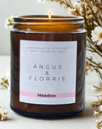 Candle in a brown jar with 'Angus & Florrie' label surrounded by flowers