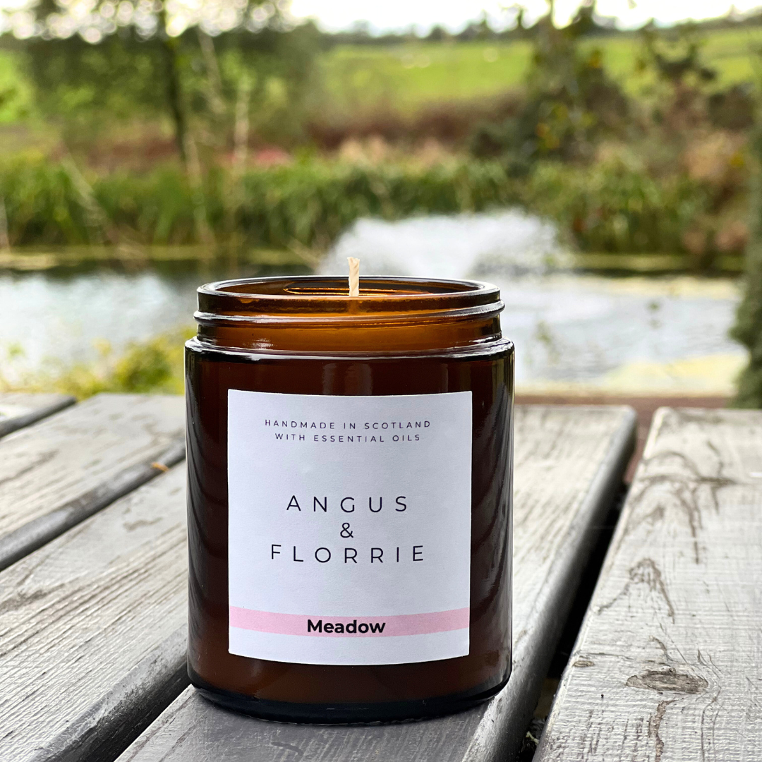 Candle in an amber jar with a label on a wooden surface, nature in the background