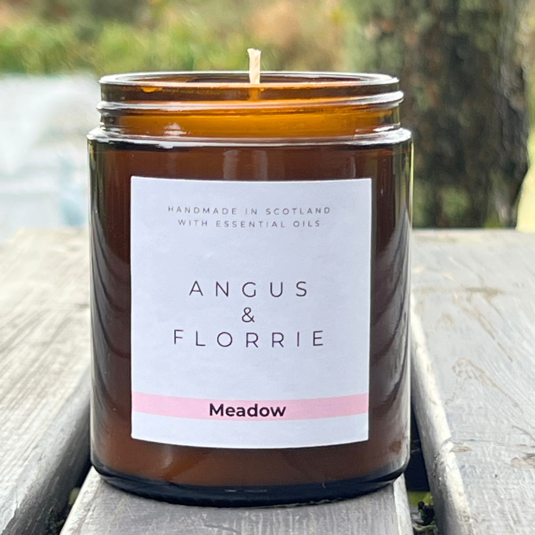 Candle in a brown jar with 'Angus & Florrie' label on a wooden surface