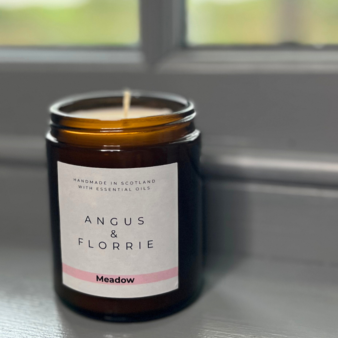 Candle in a jar with 'Angus & Florrie' label on a reflective surface