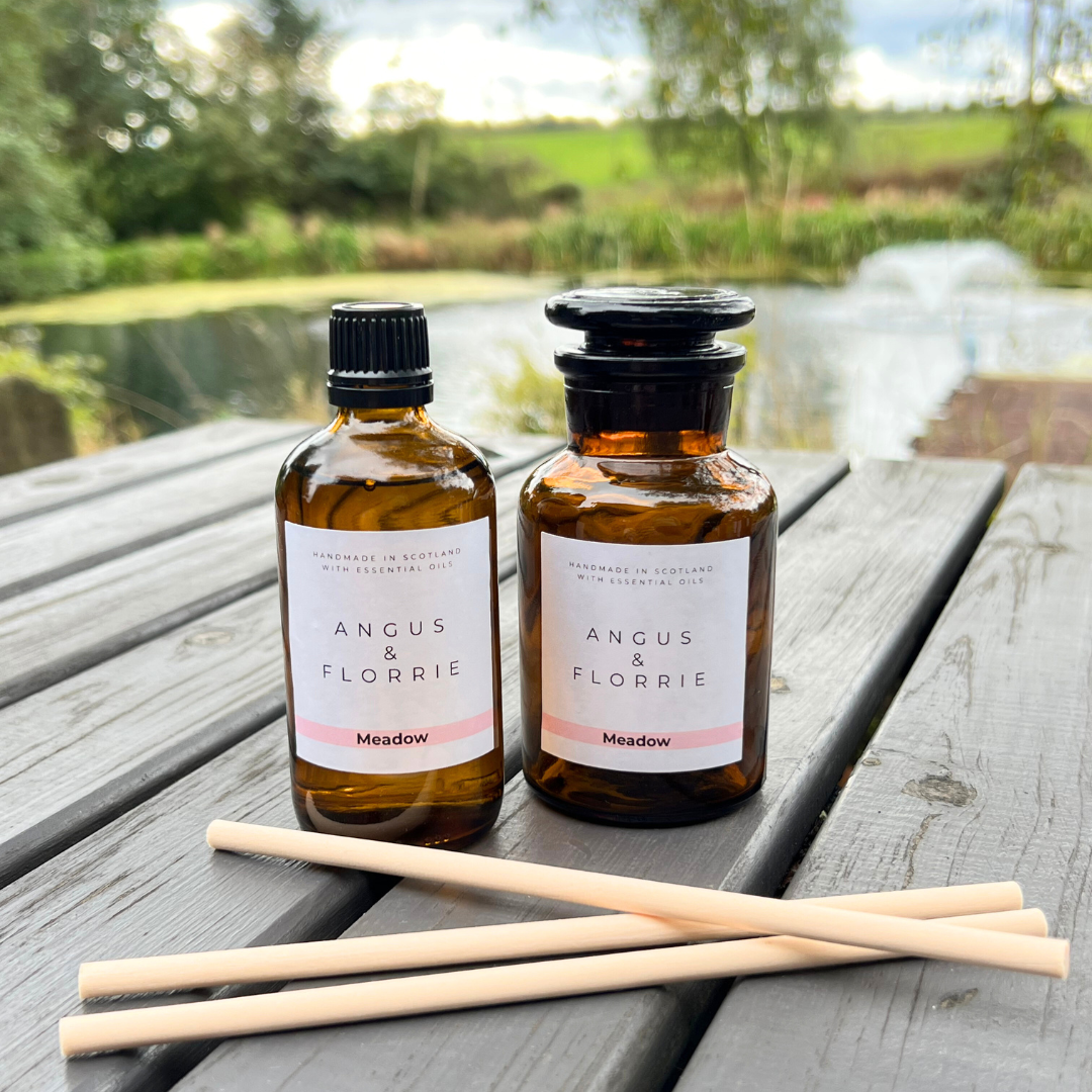 Two bottles of Angus & Florrie Meadow product on a wooden table with a scenic background.
