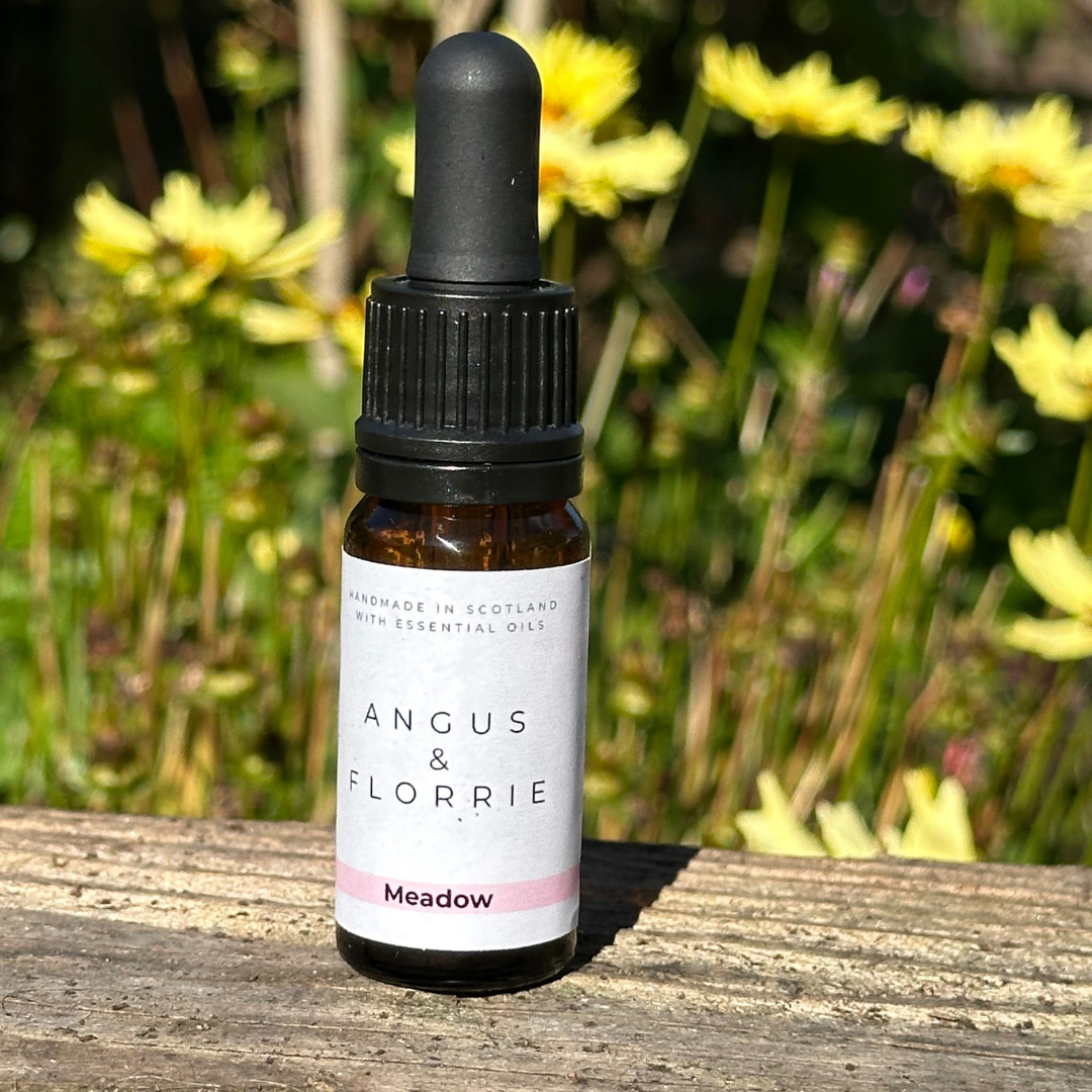 Bottle of Angus & Florrie essential oil on a wooden surface with flowers in the background