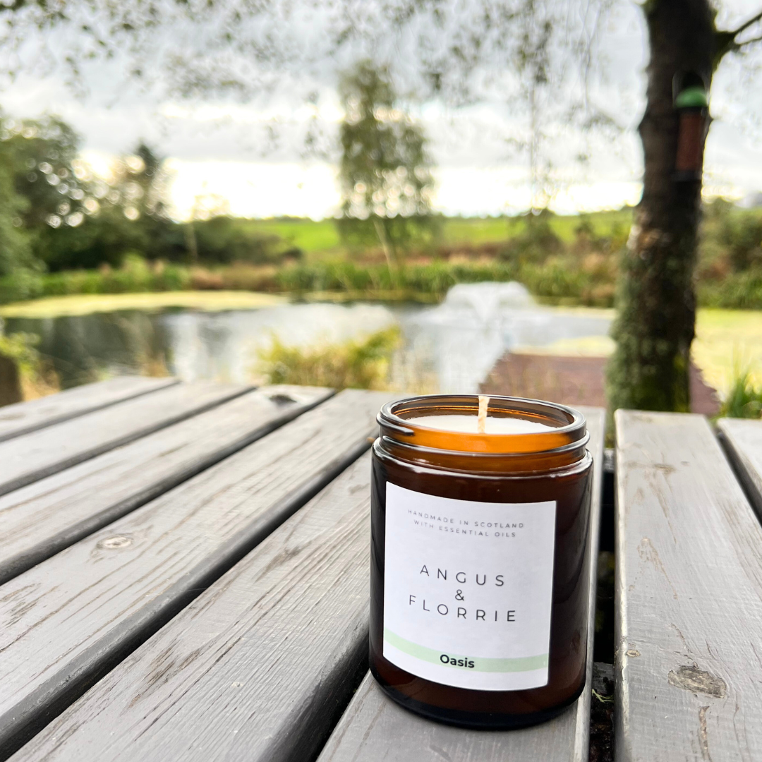 Candle in a jar labeled 'Angus & Florrie' on a wooden surface with a natural background