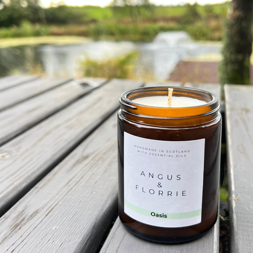 Candle in a brown jar with a label on a wooden surface, outdoors.