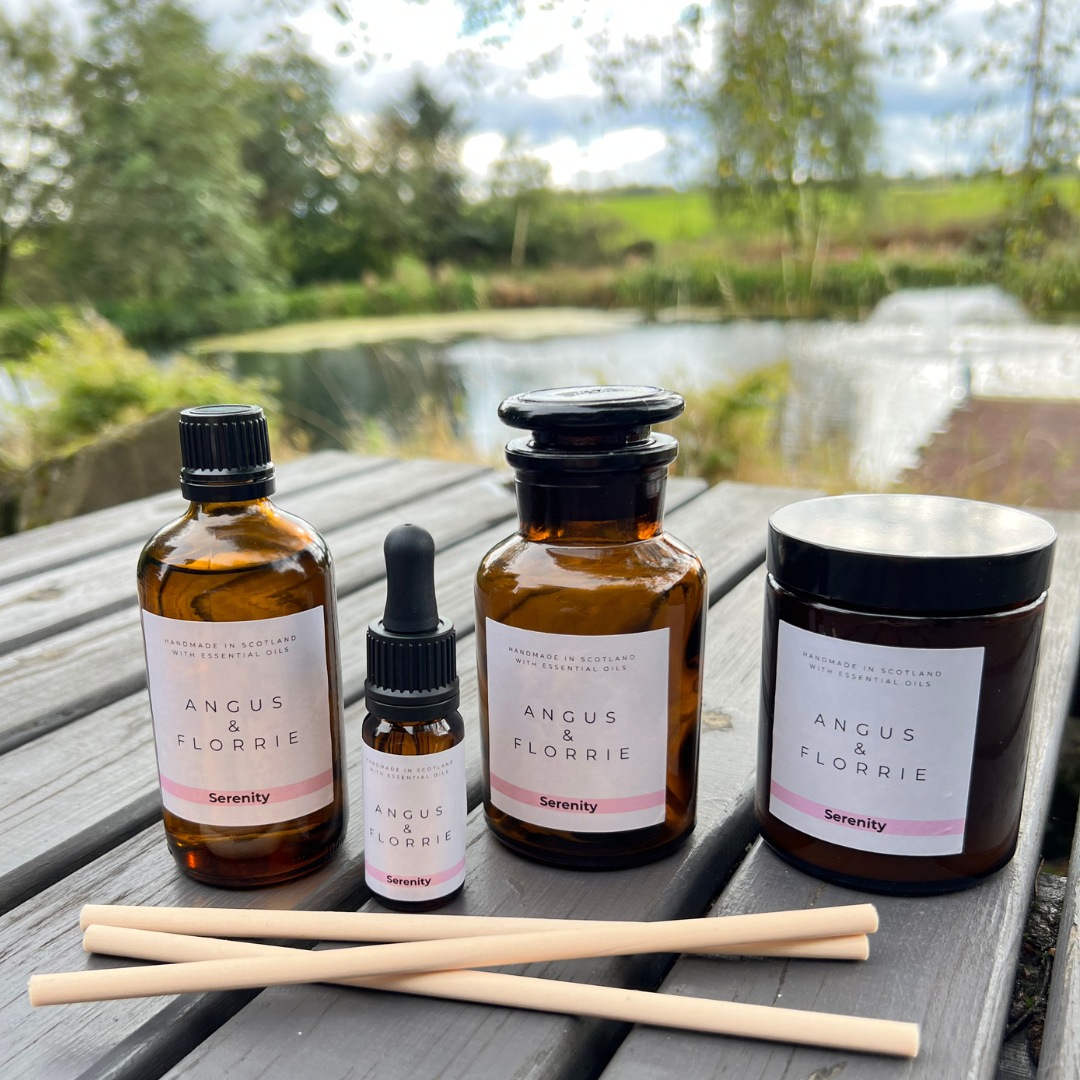Four Angus & Florrie product bottles and a candle on a wooden surface with a natural background.