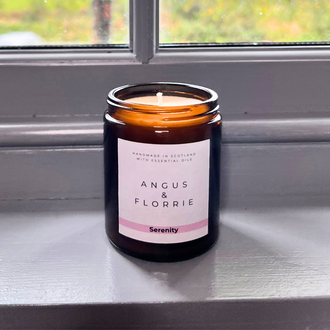 Candle in a glass jar with a label reading 'Angus & Florrie Serenity' on a reflective surface.