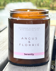 Candle in an amber jar with a label reading 'Angus & Florrie Serenity' on a wooden surface.