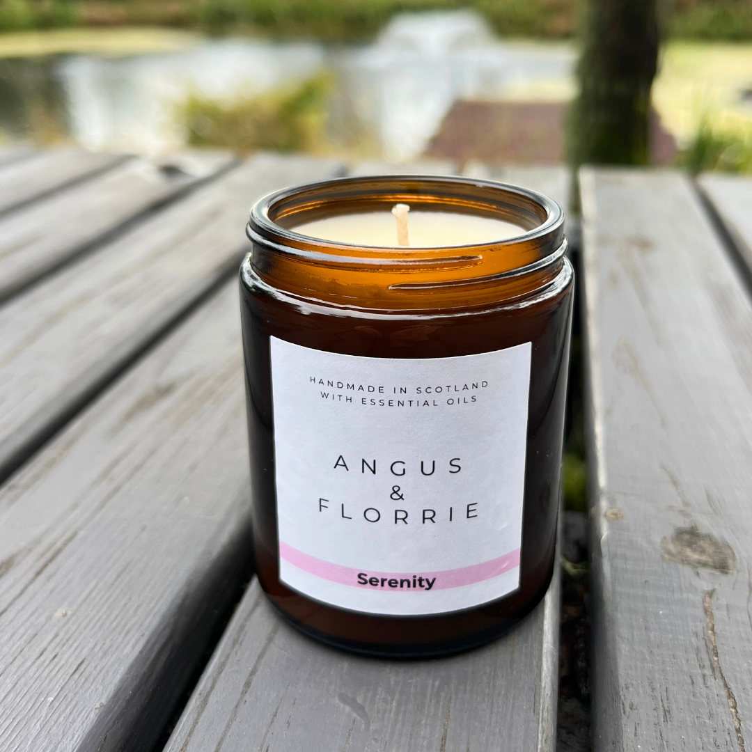 Candle in an amber jar with a label on a wooden surface outdoors