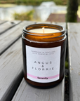 Candle in an amber jar with a label on a wooden surface outdoors