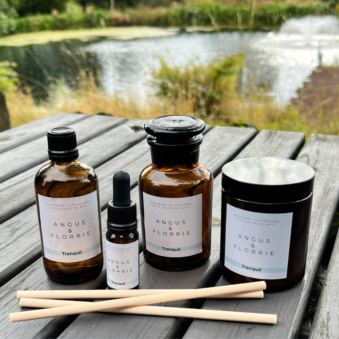 Collection of Angus & Florrie products including bottles, a candle, and sticks on a wooden surface with a natural background.